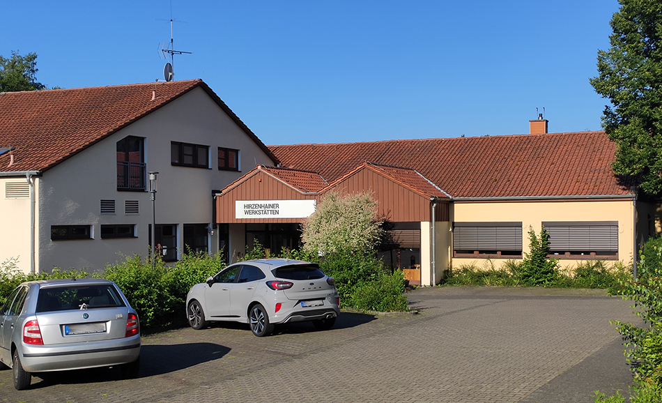 Die Hirzenhainer Werkstätten: Ein großes gelbes Haus mit einem großen Parkplatz.