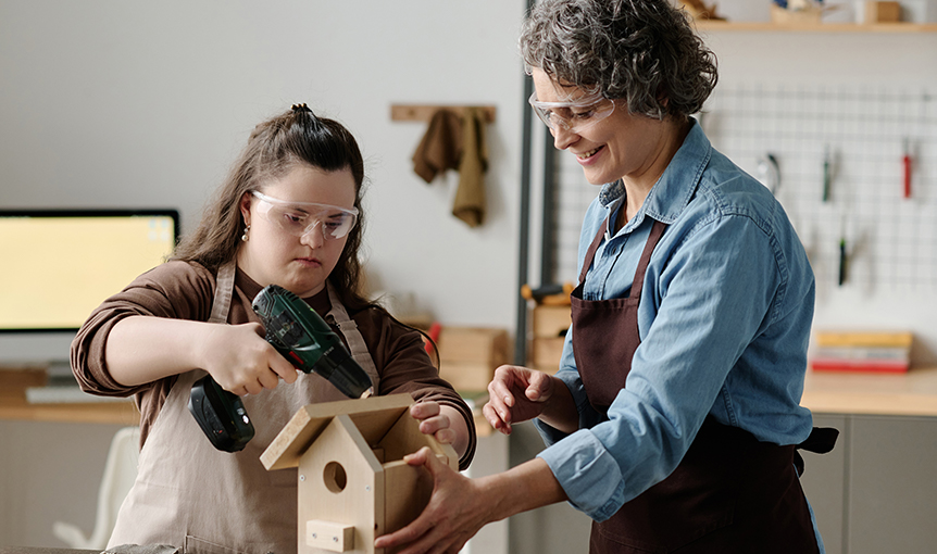 Zwei Frauen stehen in einer Schreinerei und bauen einen Nistkasten.