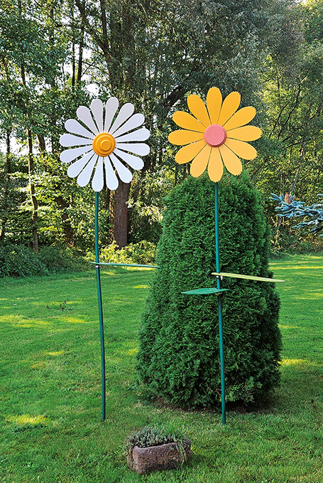 Zwei große Holzblumen stehen in einem Garten.