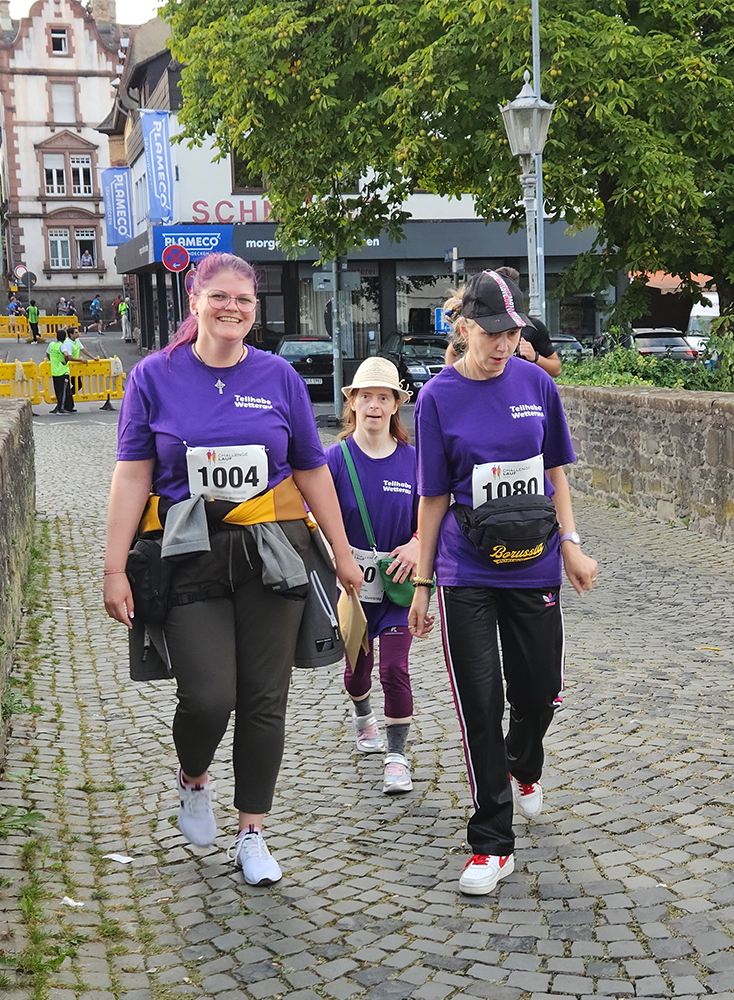 Drei Frauen in lila T-Shirts laufen beim OCL in Nidda über eine Brücke.