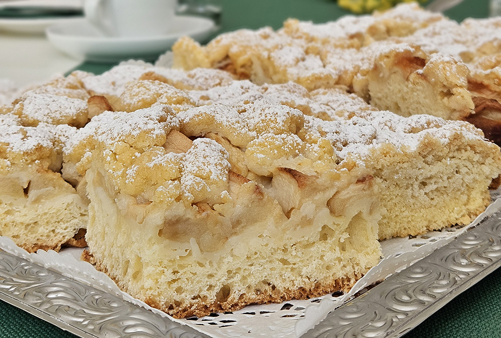 Für das Trösterkaffee wird in der Küche Blechkchen gebacken. Auf dem Bild ist ein Stück Obst-Streuselkuchen mit Puderzucker zu sehen.