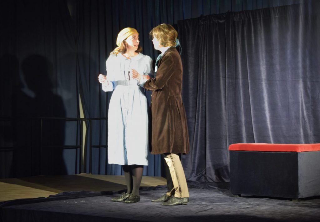 Im Theater: Gretchen mit einem hellblauen Kleid schaut naiv zu Faust, der sie am Arm hält und auf sie einredet.