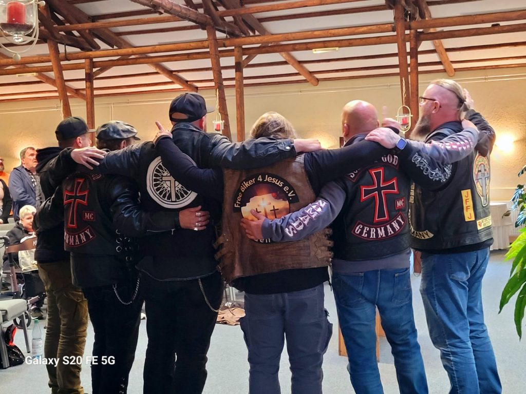 Man sieht eine Gruppe von Männern von hinten. Sie tragen Westen mit Symbolen von christlichen Motorrad-Clubs.