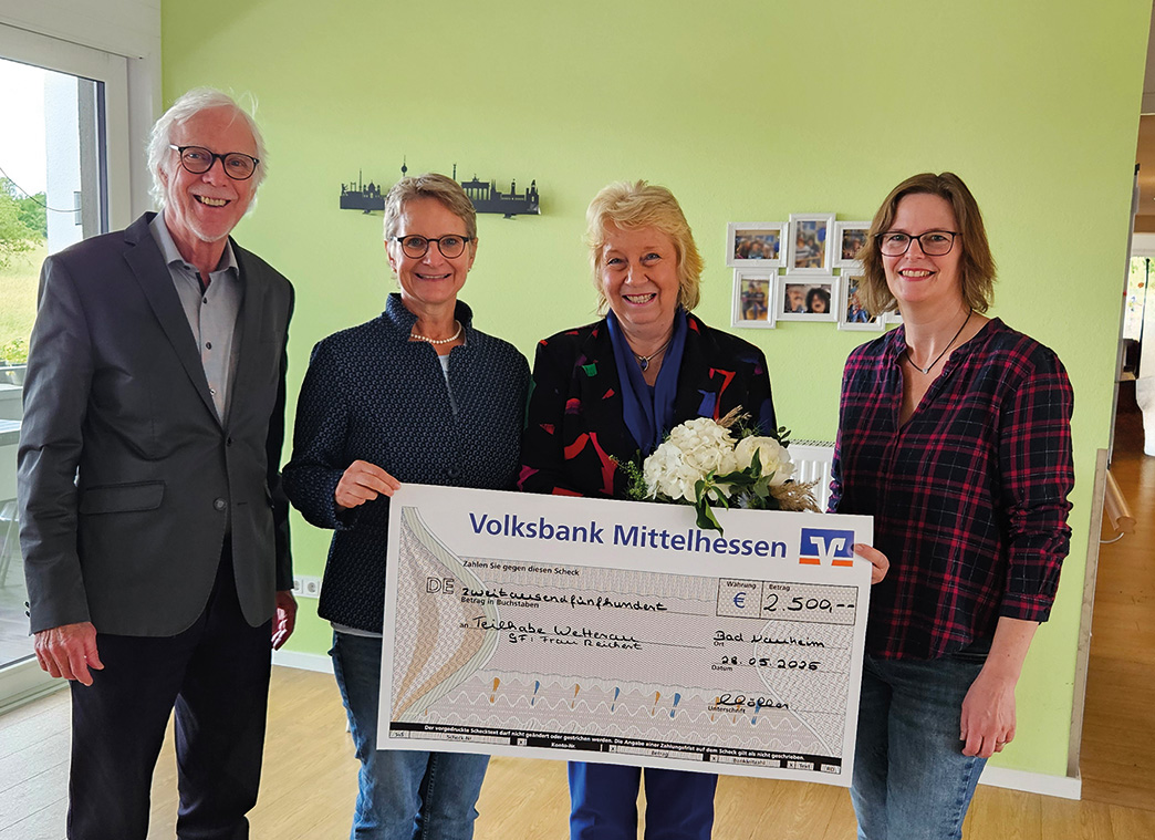 Links steht ein Mann, neben ihm drei Frauen. Alle schauen in die Kamera und lachen. Die beiden Frauen in der Mitte halten einen großen Spendenscheck vor sich auf dem steht: 2500 Euro für die Teilhabe Wetterau gGmbH.