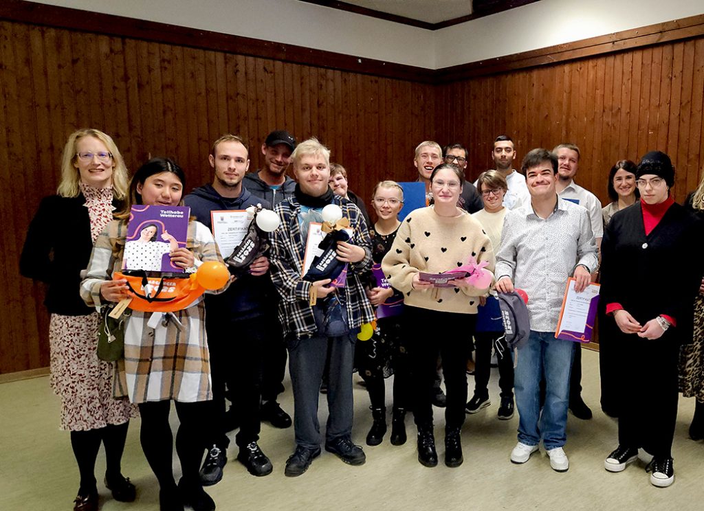 Eine Gruppe junger Menschen steht auf einer Bühne. Sie halten Abschlusszertifikate in den Händen und sehen stolz aus.