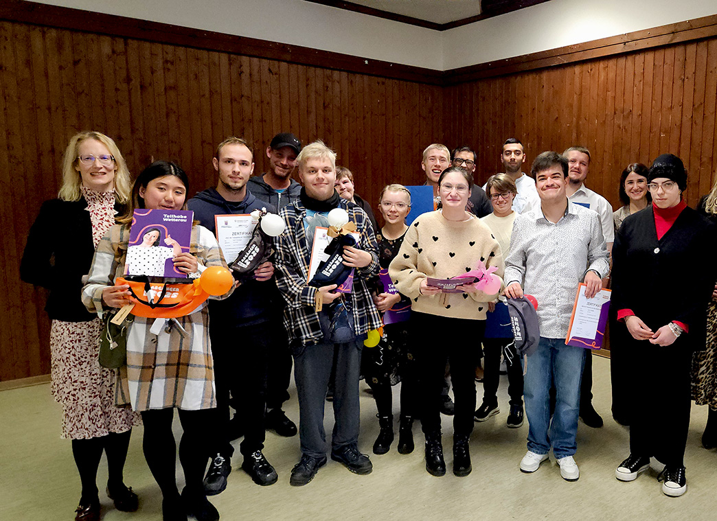 Eine Gruppe junger Menschen steht auf einer Bühne. Sie halten Abschlusszertifikate in den Händen und sehen stolz aus.