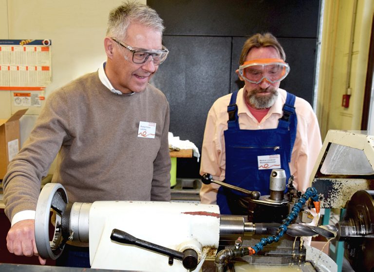 Zwei Männer stehen in einer Werkstatt hinter einer Drehmaschine und schauen die Maschine an.