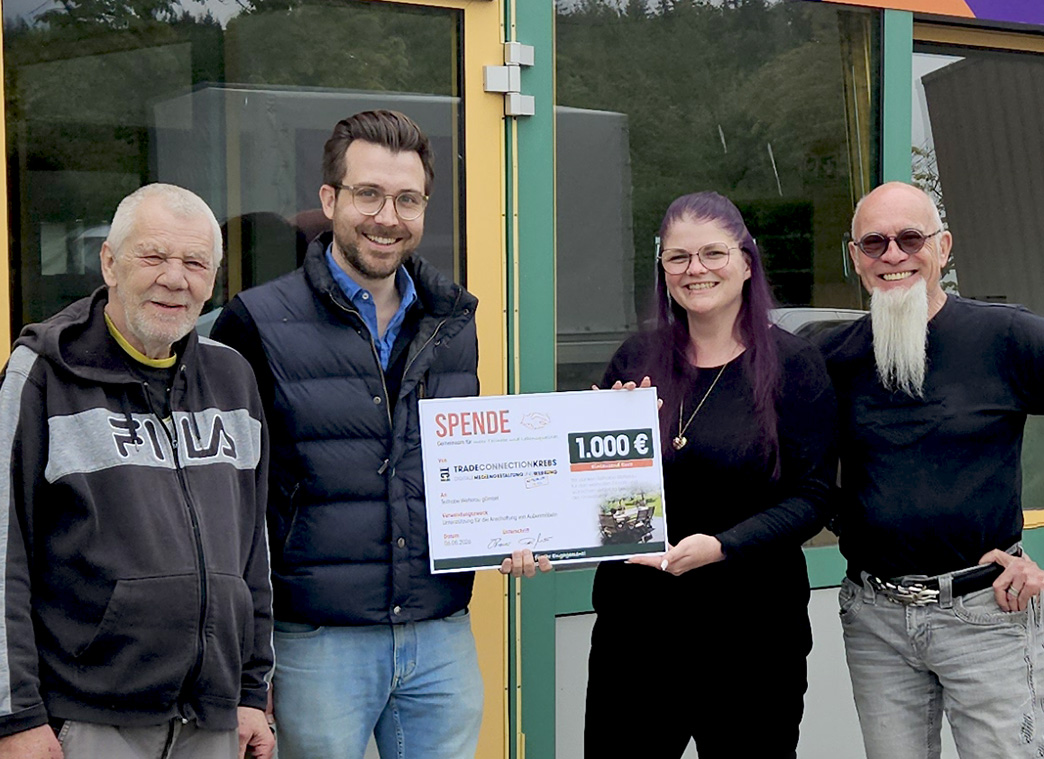 Drei Männer und eine Frau stehen nebeneinander vor dem Eingang von den Wetterauer Werkstätten. Der Mann und die Frau in der Mitte halten ein Schild. Auf dem steht: Spende und 1000 Euro.