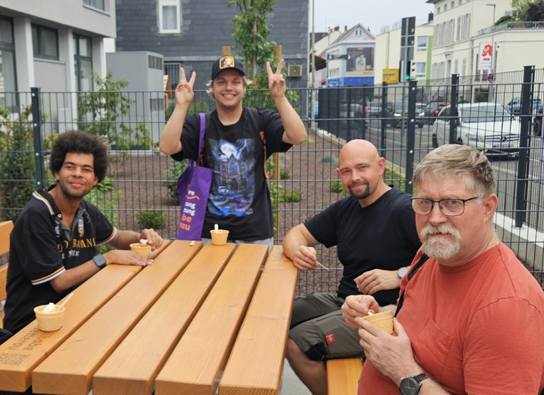 Vier Männer sitzen draußen an einem Holztisch und essen Eis